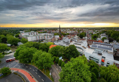 Ein Blick über das grüne Band von Elmshorn. Man sieht das Torhaus, Ramelow und die Nikolaikirche im Sonneuntergang.